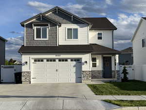 Craftsman-style home featuring a gate, concrete driveway, an attached garage, stone siding, and roof with shingles