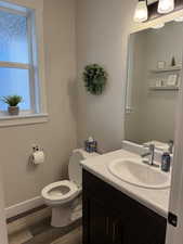 Half bathroom featuring wood finished floors, baseboards, vanity, and toilet