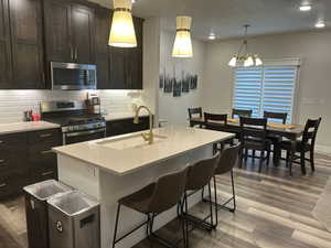 Kitchen with stainless steel appliances, a sink, decorative backsplash, wood finished floors, and a kitchen breakfast bar