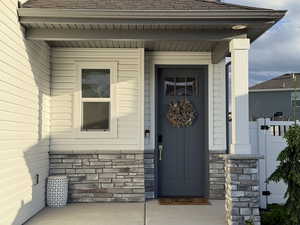 Doorway to property with stone siding, a shingled roof, and fence