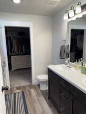 Full bath featuring a walk in closet, wood finished floors, toilet, and double vanity