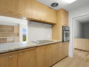 Kitchen featuring stainless steel oven, black electric cooktop, light wood-style floors, light stone counters, and light brown cabinets