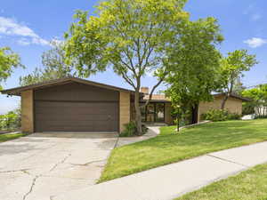 Mid-century home with brick siding, a garage, driveway, a front lawn, and a chimney