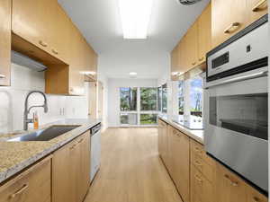Kitchen with stainless steel appliances, a sink, light wood-style floors, light stone countertops, and light brown cabinetry
