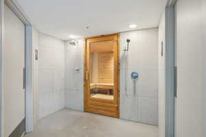 Full bathroom with finished concrete floors, tiled shower, elevator, recessed lighting, and tile walls