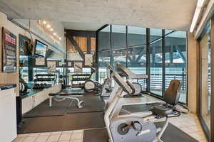 Gym with floor to ceiling windows, healthy amount of natural light, and tile patterned flooring