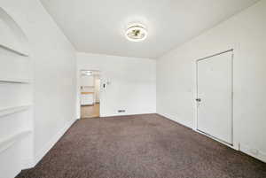 Carpeted spare room featuring built in shelves and baseboards