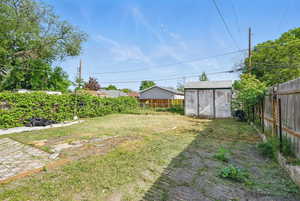 Fenced backyard featuring a shed and an outbuilding