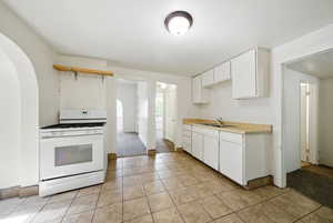 Kitchen featuring white range with gas cooktop, a sink, arched walkways, light countertops, and light tile patterned flooring