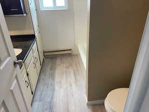 Bathroom featuring baseboard heating, wood finished floors, toilet, vanity, and a tub