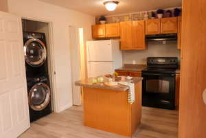 Kitchen featuring black electric range oven, under cabinet range hood, stacked washing machine and dryer, freestanding refrigerator, and light wood-style floors