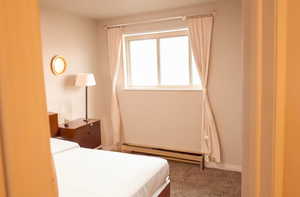Carpeted bedroom with a baseboard heating unit