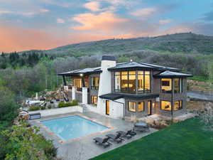 Back of house at dusk with stairs, a balcony, an outdoor pool, a patio area, and a wooded view