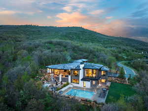 Back of house at dusk featuring stairs, a wooded view, an outdoor pool, a patio area, and a jacuzzi