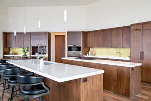Kitchen with a large island with sink, modern cabinets, a sink, a high ceiling, and tasteful backsplash