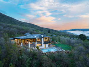 Back of property with a mountain view, an outdoor pool, a balcony, a patio, and a view of trees