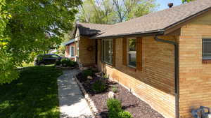 View of front walk, featuring brick siding, roof with shingles, and a yard