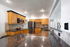 Kitchen featuring appliances with stainless steel finishes, a textured ceiling, a sink, backsplash, and dark granite counters