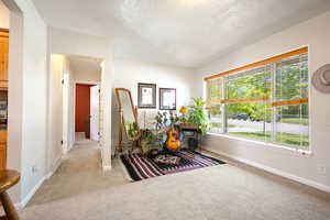 Open plan living room with large windows leading into the hallway with light colored carpet, baseboards, a textured ceiling, and attic access