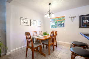 Dining space featuring a chandelier, a textured ceiling, light tile patterned floors, and baseboards