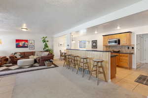 Kitchen featuring stainless steel microwave, a breakfast bar, open floor plan, dark countertops, and a textured ceiling