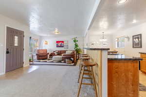 Main living area with bar seating, light carpet, light tile patterned floors, and a chandelier