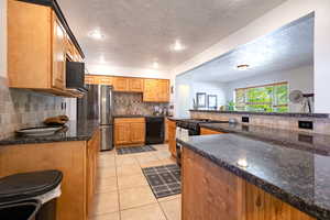 Kitchen with black appliances, tasteful backsplash, light tile patterned flooring, a textured ceiling, and dark granite counters