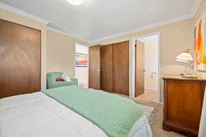 Bedroom featuring light colored carpet, crown molding, two closets, and baseboards