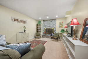 Living room with recessed lighting, light colored carpet, a stone fireplace, a textured ceiling, and baseboards