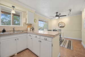 Kitchen featuring a peninsula, tile counters, a sink, a ceiling fan, and white cabinetry