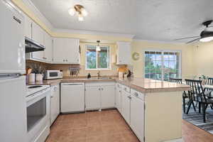 Kitchen with white appliances, under cabinet range hood, a peninsula, tile counters, and white cabinets