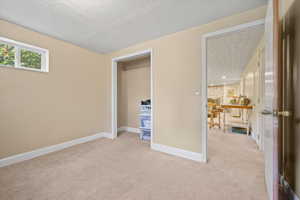 Unfurnished bedroom with light colored carpet, a textured ceiling, and baseboards