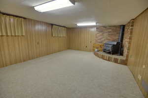 Finished below grade area with carpet, a wood stove, and wooden walls