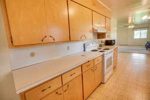 Kitchen featuring electric range, under cabinet range hood, light countertops, open floor plan, and a ceiling fan