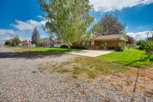 View of green lawn with concrete driveway and a carport