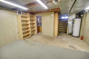 Unfinished below grade area with gas water heater, stairs, and wooden walls