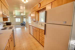 Kitchen featuring white appliances, a chandelier, under cabinet range hood, a sink, and light countertops