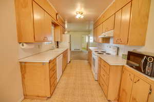 Kitchen featuring white appliances, under cabinet range hood, light countertops, and light flooring