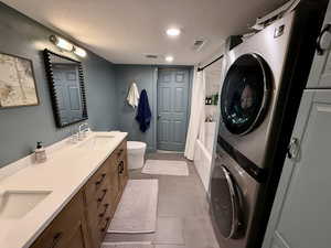 Full bath with stacked washer / dryer, a textured ceiling, toilet, double vanity, and shower / tub combo with curtain