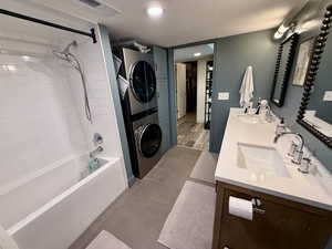 Full bath featuring stacked washer / dryer, double vanity, shower / bath combination, and tile patterned flooring