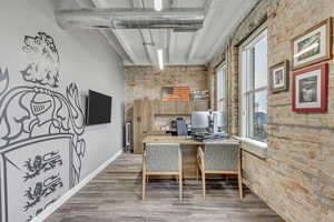 Office area featuring brick wall, wood finished floors, beam ceiling, and baseboards