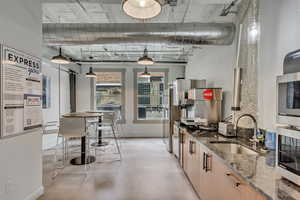 Kitchen with a sink, dark stone countertops, stainless steel microwave, baseboards, and finished concrete floors