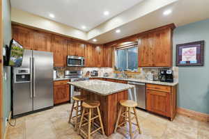 Kitchen with appliances with stainless steel finishes, brown cabinets, a kitchen breakfast bar, decorative backsplash, and recessed lighting