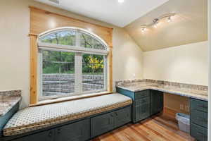 Unfurnished office with light wood finished floors, vaulted ceiling, and built in desk