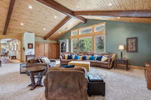 Carpeted living room with wood ceiling, beam ceiling, recessed lighting, arched walkways, and baseboards