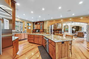 Kitchen with a sink, light wood finished floors, a breakfast bar area, stainless steel dishwasher, and arched walkways