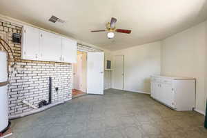Kitchen with a ceiling fan, white cabinetry, a brick fireplace, and baseboards
