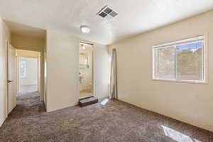 Unfurnished bedroom featuring carpet floors, a textured ceiling, and ensuite bathroom