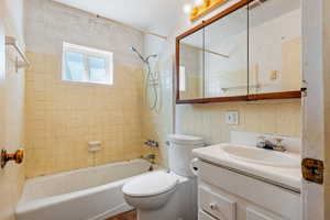 Full bathroom with bathing tub / shower combination, toilet, vanity, and tile walls