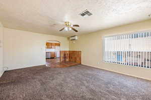 Empty room featuring arched walkways, a wall unit AC, carpet, a ceiling fan, and a textured ceiling